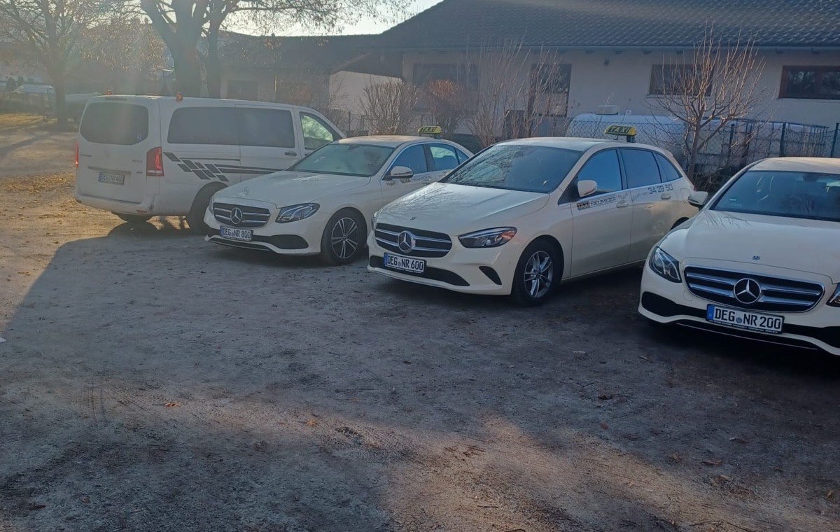 The fleet of Taxi Neumeier: four light-coloured Mercedes taxis and a Vito people carrier in the morning sun